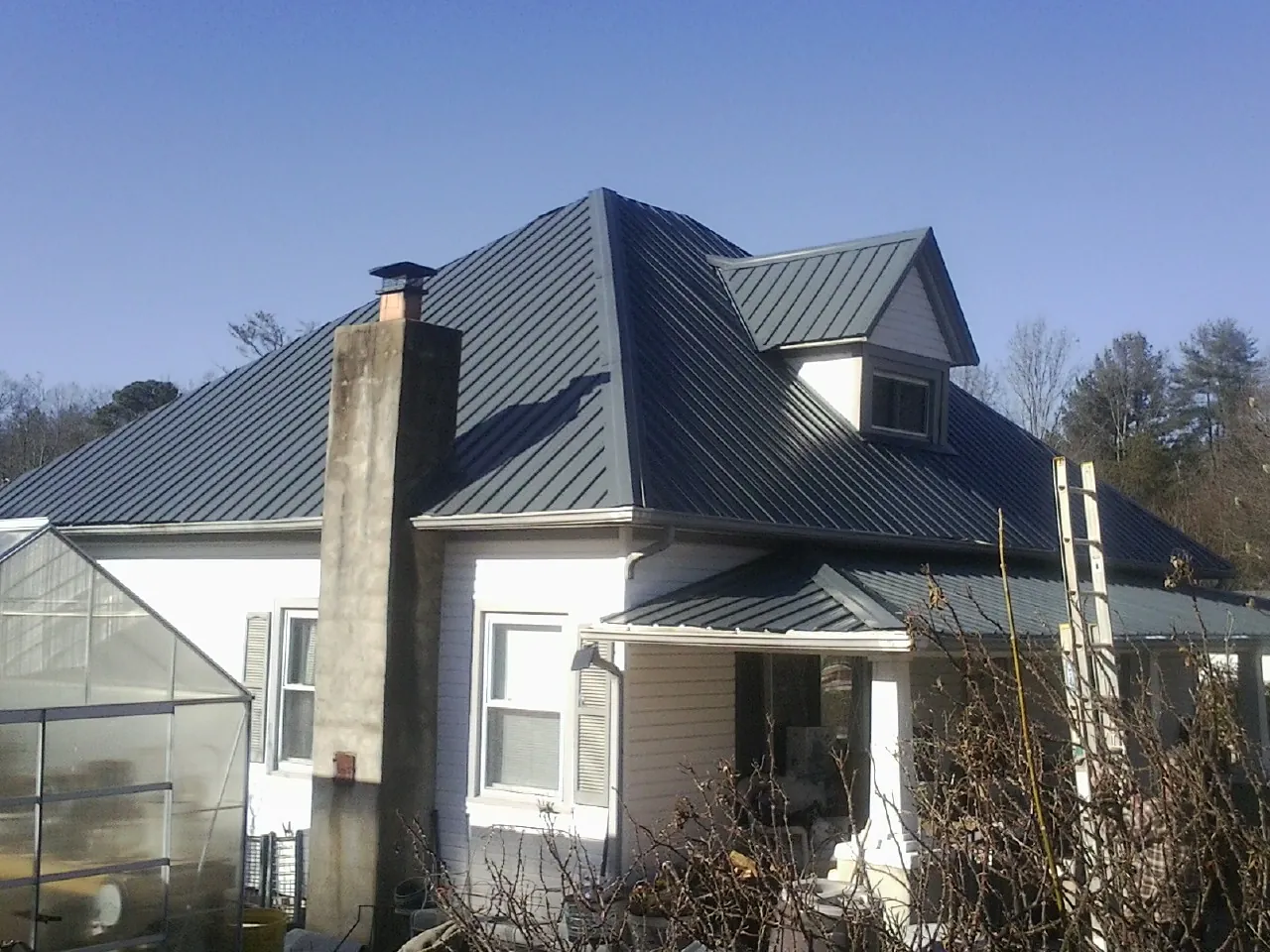 Dark blue standing seam metal roof on a white farmhouse with dormer — Slate & Tile Roof Repair by Roofing Brothers in Alma