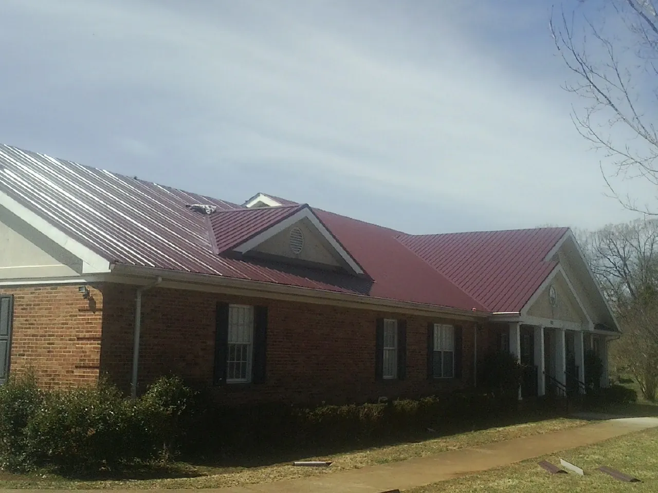 Red metal roof with gabled entries on a long brick building, from a Hail Damage Roof Repair job in Alma