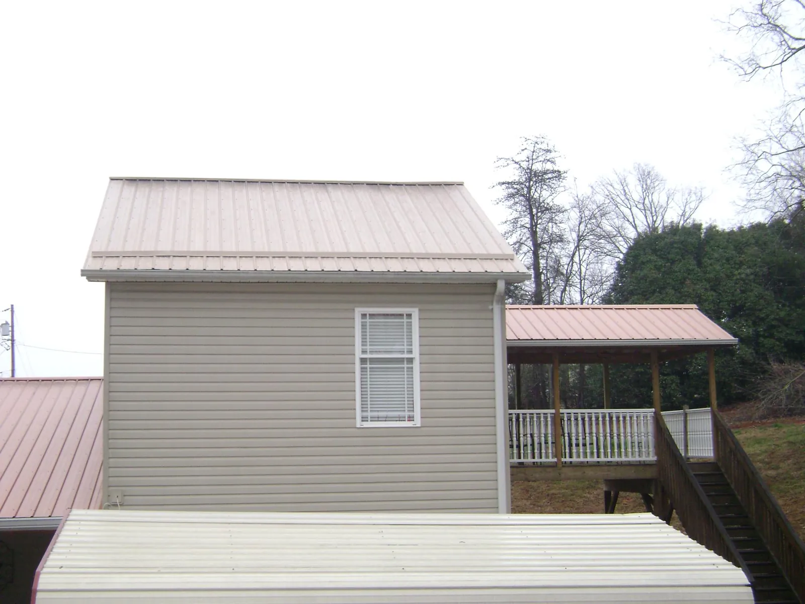 Tan metal roofs on a two story addition and attached porch, from a Roof Replacement job in Alma